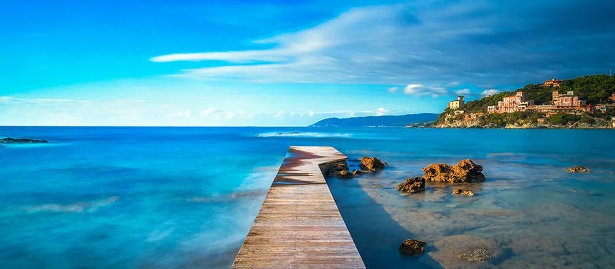 Ein hölzerner Steg an einem Strand auf der Insel Elba mit Blick auf das klare, türkisfarbene Meer.
